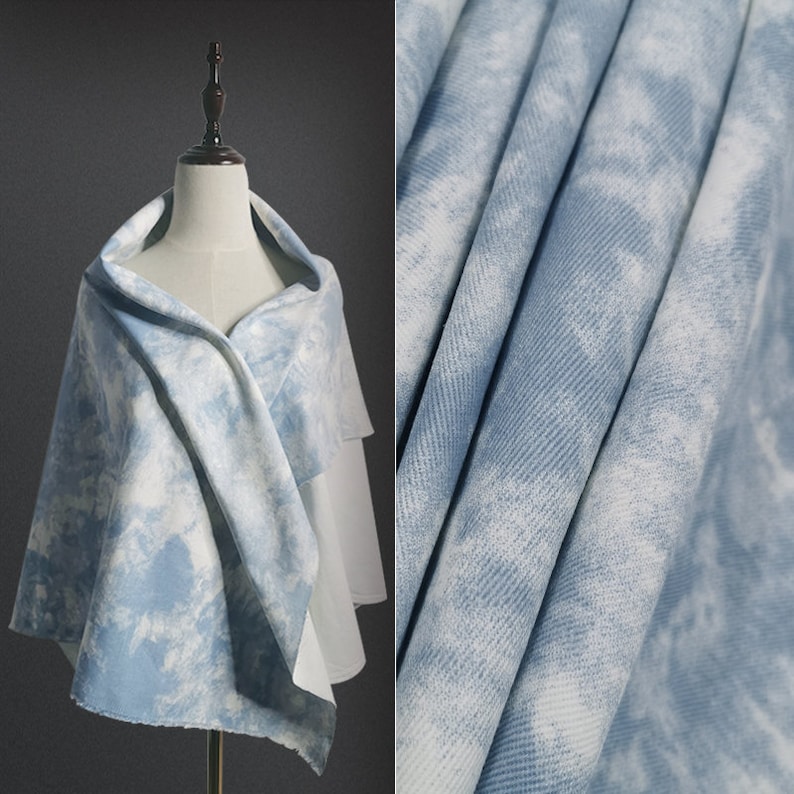 Pu&ograve; includere: Un tessuto tie-dye blu chiaro su sfondo bianco. Il tessuto &egrave; piegato e drappeggiato su un manichino.