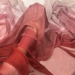 K&ouml;nnte beinhalten: Ein durchsichtiger Stoff mit einem Farbverlauf von Rosa, Rot und Orange. Der Stoff ist drapiert und gefaltet, wodurch ein weicher und flie&szlig;ender Look entsteht.