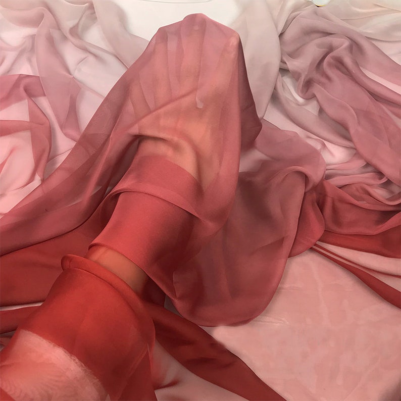 K&ouml;nnte beinhalten: Ein durchsichtiger Stoff mit einem Farbverlauf von Rosa, Rot und Orange. Der Stoff ist drapiert und gefaltet, wodurch ein weicher und flie&szlig;ender Look entsteht.