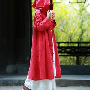 May include: A long, red hooded coat with a button fastening. The coat is made from a lightweight fabric and has a relaxed fit.