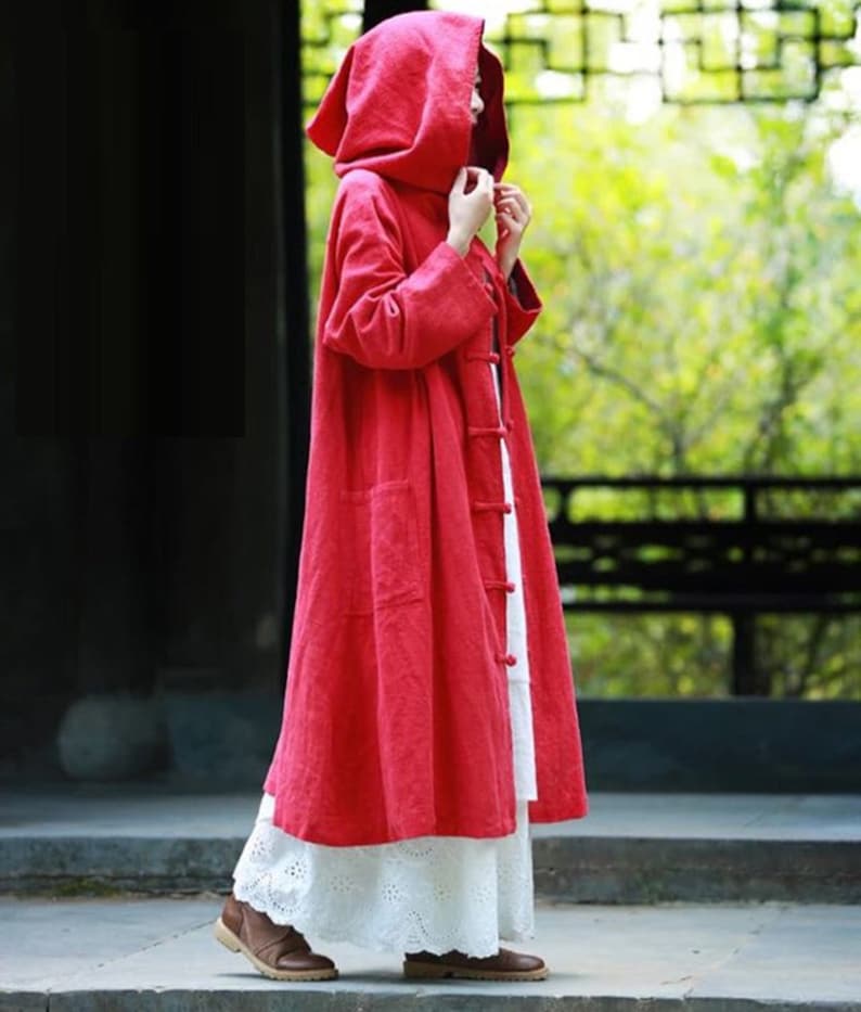 May include: A long, red hooded coat with a button fastening. The coat is made from a lightweight fabric and has a relaxed fit.