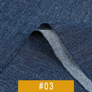 May include: Close-up of a dark blue denim fabric with a textured weave. The fabric is folded over, revealing the underside of the material. The image is labeled with the number #03.