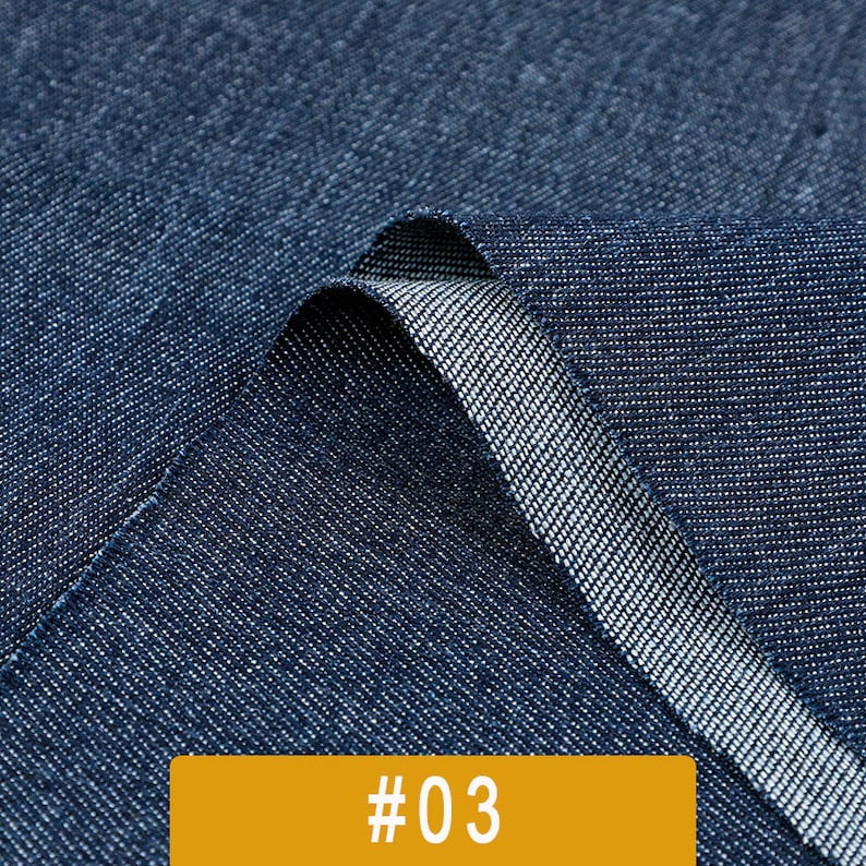 May include: Close-up of a dark blue denim fabric with a textured weave. The fabric is folded over, revealing the underside of the material. The image is labeled with the number #03.