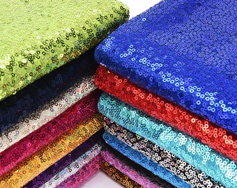 Puede incluir: Una pila de tela de lentejuelas en varios colores, incluyendo verde, azul, rojo, dorado, turquesa y morado. La tela está hecha de lentejuelas cosidas sobre un respaldo de malla.
