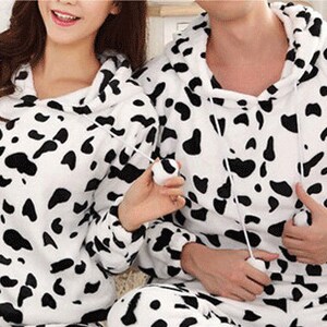 May include: A pair of matching pajamas with a black and white cow print pattern. The pajamas have a hooded top and long sleeves.