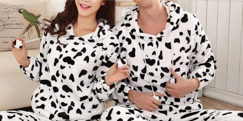 May include: A pair of matching pajamas with a black and white cow print pattern. The pajamas have a hooded top and long sleeves.