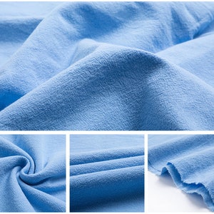 May include: Close-up of a light blue fabric with a textured surface. The fabric is soft and has a slightly wrinkled appearance.