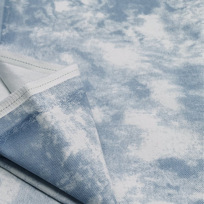 Pu&ograve; includere: Primo piano di un tessuto denim blu chiaro con un motivo tie-dye bianco. Il tessuto ha una texture sottile e un aspetto morbido e sbiadito.