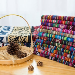 May include: A stack of colorful fabric with geometric patterns. The fabric is woven with stripes and intricate designs in shades of red, blue, green, yellow, and brown.