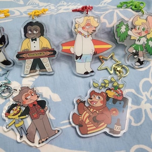 Könnte beinhalten: Ein Set mit zehn bunten Schlüsselanhängern mit Comic-Tierfiguren. Die Schlüsselanhänger sind aus klarem Acryl und haben verschiedene Designs, darunter ein Hund, der Keyboard spielt, ein Bär, der Gitarre spielt, ein Wolf mit einer Puppe, eine Maus mit Pompons, ein Eisbär, der ein Surfbrett hält, und ein Hund, der einen Raumanzug trägt.