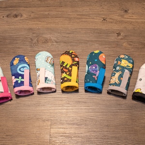 May include: Eight colorful fingertip protectors with different patterns, including a cat, a pineapple, a sun, a fish, a bird, a cloud, and a geometric design.