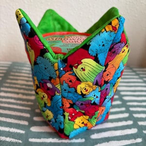 Op de afbeelding: Een groene en zwarte stoffen container met een kleurrijke print van cartoonhonden. De container is ontworpen om een cilindrisch voorwerp te bevatten, zoals een blik of een pot.