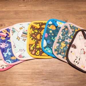 May include: Set of eight colorful pot holders with various patterns, including a llama, avocado, fish, cats, and farm animals. The pot holders are quilted and have a contrasting trim.
