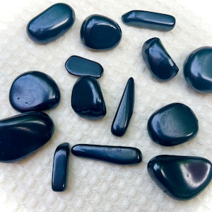Könnte beinhalten: Eine Sammlung von 12 glatten, schwarzen Obsidian-Steinen in verschiedenen Formen und Größen. Die Steine sind poliert und haben eine glänzende Oberfläche.