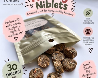 May include: A gold-colored resealable pouch labeled Hammy Niblets containing 30 round, textured treats made of nuts, seeds, raspberry, apple, and mealworms. The packaging features text including Cozy Indoor Critters, 100% natural ingredients, and Small Treats. Big Happiness.