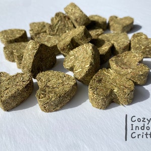 May include: A pile of heart-shaped green hay pellets for small animals. The pellets are made of compressed grass and are a healthy treat for pets.