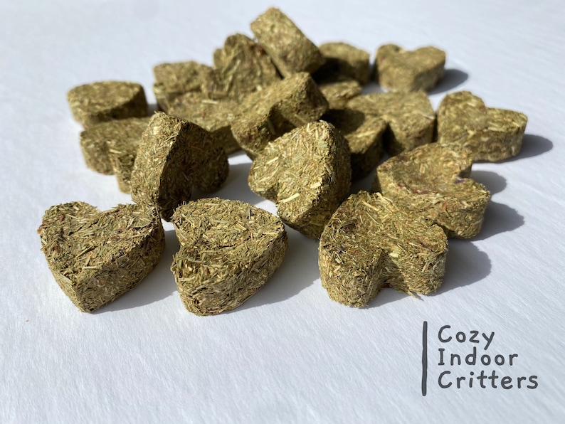 May include: A pile of heart-shaped green hay pellets for small animals. The pellets are made of compressed grass and are a healthy treat for pets.