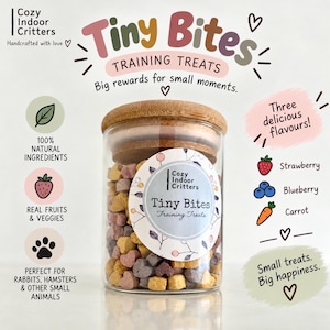 May include: A clear glass jar with a bamboo lid filled with heart-shaped pet treats. The label reads Tiny Bites Training Treats. Surrounding text highlights 100% natural ingredients, real fruits and veggies, and three flavors: strawberry, blueberry, and carrot.