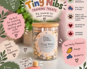 May include: A clear glass jar with a bamboo lid filled with small, cube-shaped pet treats labeled Tiny Nibs Training Treats. The label features the text Cozy Indoor Critters. A single tan treat is held in the foreground, with text surrounding the jar detailing natural ingredients, fruit and vegetable content, and suitability for small animals.