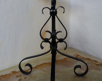 May include: Black metal candle holder with a twisted stem and ornate scrollwork details. The holder has a round top and three legs.