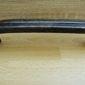 Könnte beinhalten: Ein schwarzer Türgriff aus Metall mit gebogenem Design. Der Griff besteht aus zwei miteinander verbundenen Metallteilen.