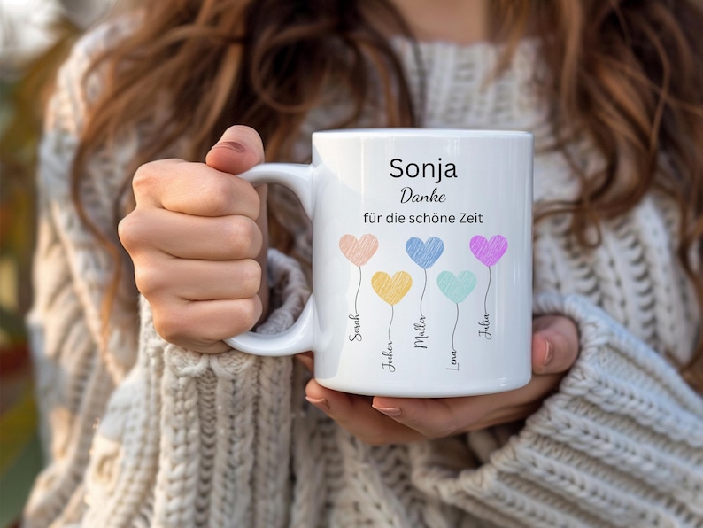 May include: White ceramic mug with the name "Sonja" and the German phrase "Danke f&uuml;r die sch&ouml;ne Zeit." The mug features four colourful heart-shaped balloons with names below. The mug is held by a person wearing a cream-coloured sweater.