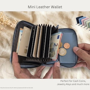 Könnte beinhalten: Ein blaues Mini-Lederportemonnaie, geöffnet, um Karten, Bargeld und Münzen zu zeigen. Das Portemonnaie ist mit einem Reißverschluss versehen und hat mehrere Kartenfächer. Der Text "Mini Leather Wallet" steht oben. Mehrere andere farbige Geldbörsen werden angezeigt.