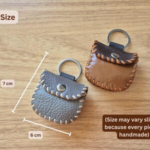 May include: Handmade leather keychains in brown and gray, each measuring approximately 2.4 inches wide and 2.8 inches tall. The keychains feature a stitched design and a metal keyring. The text on the image says "Size may vary slightly because every piece is handmade."