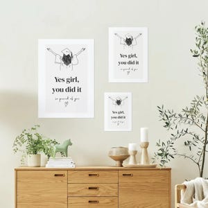 Peut inclure: Trois impressions d'art encadr&eacute;es avec le texte "Yes girl, you did it" dans un design minimaliste. Les impressions pr&eacute;sentent une illustration de chapeau de graduation. L'&oelig;uvre est affich&eacute;e au-dessus d'un meuble en bois avec des objets d&eacute;coratifs.