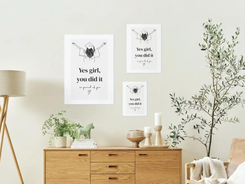 Peut inclure: Trois impressions d'art encadr&eacute;es avec le texte "Yes girl, you did it" dans un design minimaliste. Les impressions pr&eacute;sentent une illustration de chapeau de graduation. L'&oelig;uvre est affich&eacute;e au-dessus d'un meuble en bois avec des objets d&eacute;coratifs.