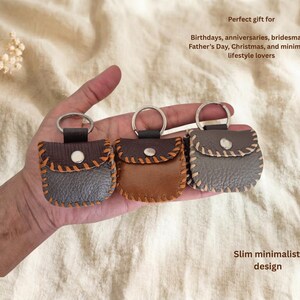 May include: Three small leather keychains in shades of brown and gray, each with a silver ring. The keychains have a stitched design and a button closure. Text on the image reads: "Perfect gift for Birthdays, anniversaries, bridesmaids, Father's Day, Christmas, and minimalist lifestyle lovers" and "Slim minimalist design."