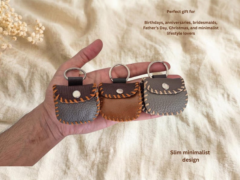 May include: Three small leather keychains in shades of brown and gray, each with a silver ring. The keychains have a stitched design and a button closure. Text on the image reads: "Perfect gift for Birthdays, anniversaries, bridesmaids, Father's Day, Christmas, and minimalist lifestyle lovers" and "Slim minimalist design."