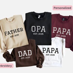 Peut inclure: Cinq sweat-shirts brodés de différentes couleurs avec les mots "Father", "Opa", "Papa", "Dad" et "Papa" avec l'année "EST. 2025" sous chaque mot.