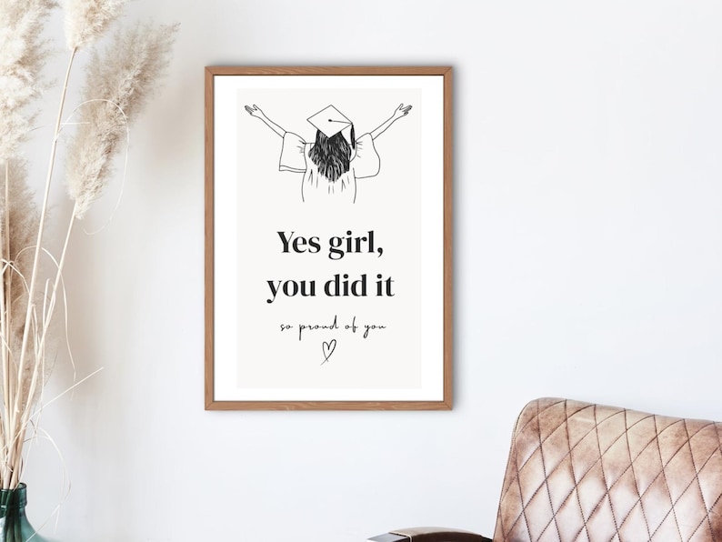 Peut inclure: Une affiche encadr&eacute;e avec une illustration minimaliste d'une dipl&ocirc;m&eacute;e en chapeau et robe, les bras lev&eacute;s. L'affiche porte l'inscription "Yes girl, you did it, so proud of you" dans une police &eacute;l&eacute;gante. Le cadre est marron chaud.