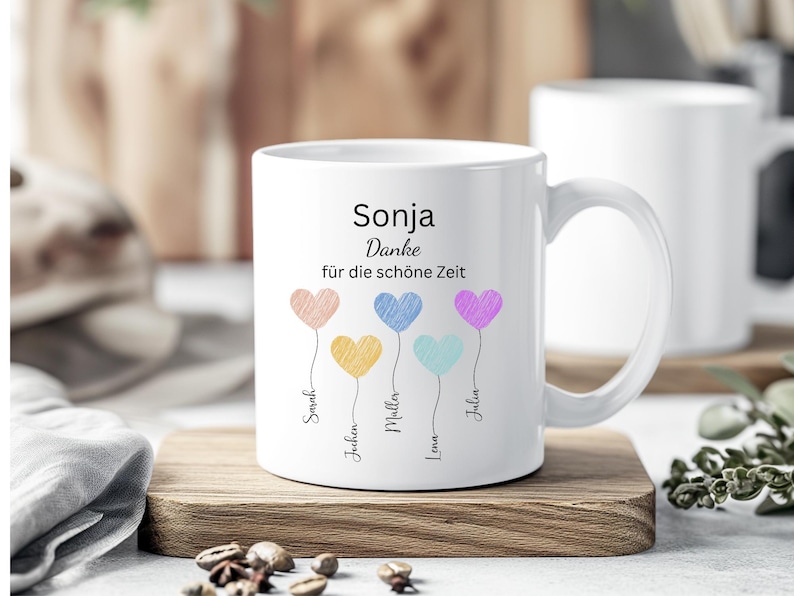May include: White ceramic mug with a handle, featuring the name "Sonja" and the phrase "Danke f&uuml;r die sch&ouml;ne Zeit." Colorful heart-shaped balloons with names below them decorate the mug. The mug sits on a wooden surface.