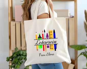 May include: White tote bag with a design of colorful school supplies, including pencils, crayons, a ruler, and a paintbrush. The text "Lehrerin Frau Elena" is printed on the bag.
