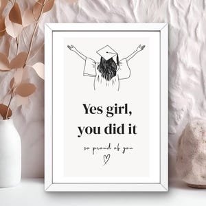 Peut inclure: Impression encadr&eacute;e blanche avec un dessin au trait d'une personne en chapeau de graduation, les bras lev&eacute;s. Le texte dit "Yes girl, you did it, so proud of you" avec un symbole de c&oelig;ur.