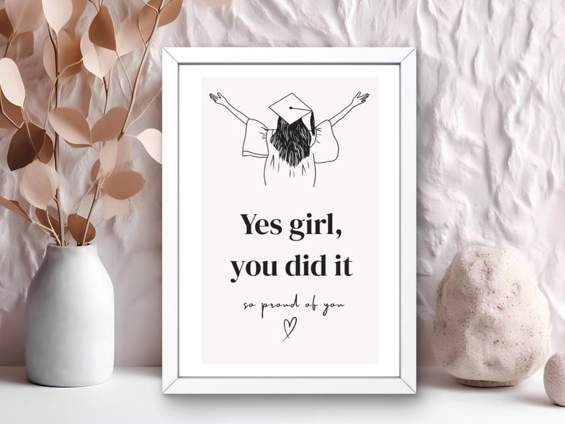 Peut inclure: Impression encadr&eacute;e blanche avec un dessin au trait d'une personne en chapeau de graduation, les bras lev&eacute;s. Le texte dit "Yes girl, you did it, so proud of you" avec un symbole de c&oelig;ur.