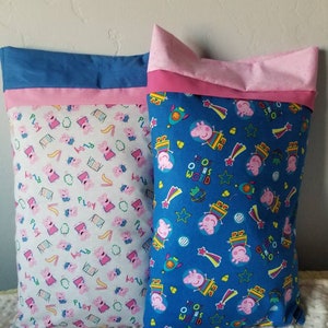 May include: Two rectangular pillowcases. One is white with a pink Peppa Pig pattern and the word "PLAY". The other is blue with a Peppa Pig space theme and the words "OHS WORLD". Both have pink and blue trim.