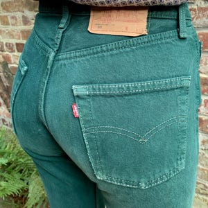 Op de afbeelding: Een paar donkergroene spijkerbroeken met een achterzak met een rood Levi's-label en witte stiksels. De broek heeft een hoge taille en een rechte pijp.