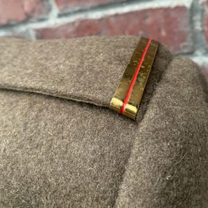 May include: A close-up of a brown wool jacket with a gold and red shoulder patch.
