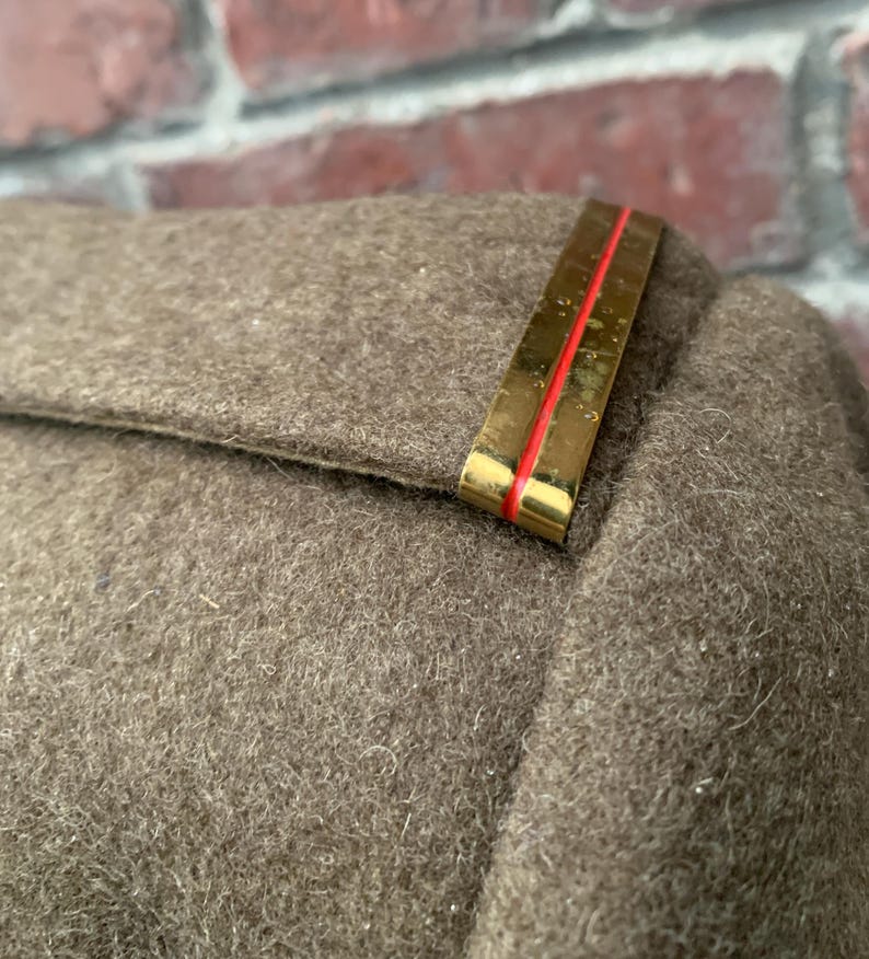 May include: A close-up of a brown wool jacket with a gold and red shoulder patch.