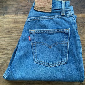 May include: A pair of blue denim jeans with a brown leather Levi's patch on the back waistband. The jeans have a back pocket with a red Levi's tab.
