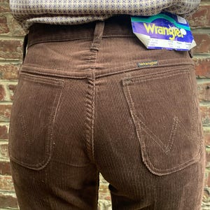 Könnte beinhalten: Braune Cordhose mit einem Wrangler-Etikett auf der Gesäßtasche. Die Hose hat eine weite Beinweite und eine hohe Taille.