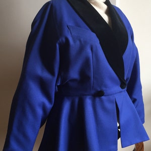 May include: A blue blazer with a black velvet collar. The blazer has a fitted bodice and a flared skirt.