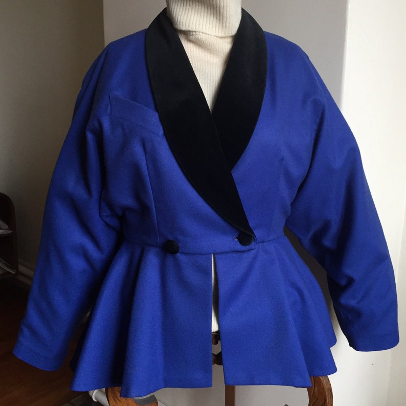 May include: A blue blazer with a black velvet collar. The blazer has a peplum hem and two buttons at the waist.