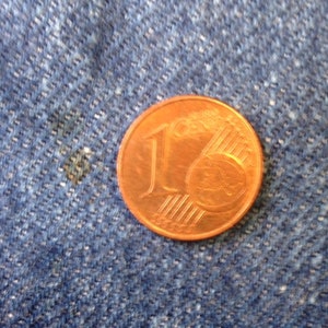 May include: A copper-colored one-cent Euro coin featuring the numeral one and a globe graphic with six parallel lines. The coin is circular with a smooth edge and displays the text 1 Euro Cent clearly on its metallic surface.
