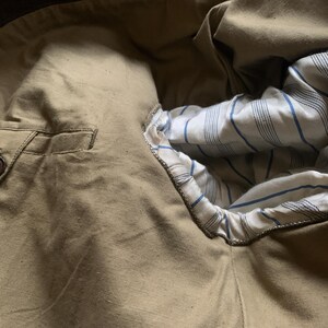 May include: A close-up of the inside of a brown jacket, showing the lining with a white and blue striped pattern.