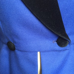 May include: A blue blazer with a black velvet collar and two black buttons. The blazer has a single gold button on the front.