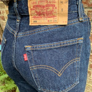 May include: A pair of dark blue denim jeans with a brown leather Levi's patch that reads "Levi Strauss & Co. Original Riveted Quality Clothing XX" and "501 W27 L34".